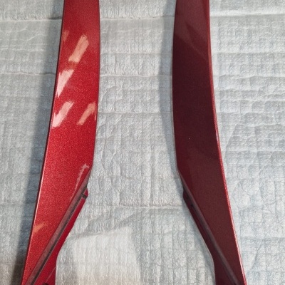 Dois elementos vermelhos metálicos alongados sobre tecido cinza acolchoado