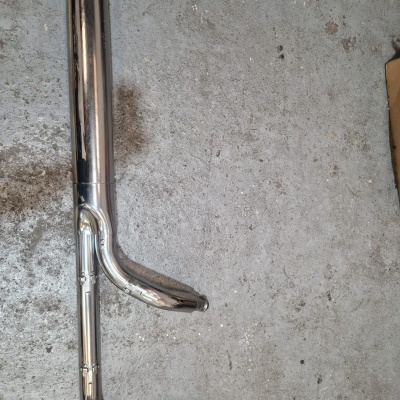 Peça metálica tubular cromada com curvas sobre chão cinzento
