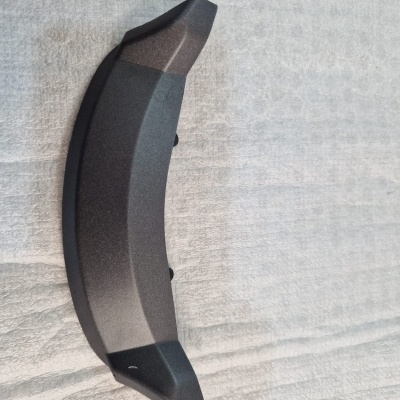 Peça de automóvel preta curvada sobre superfície acolchoada cinza clara