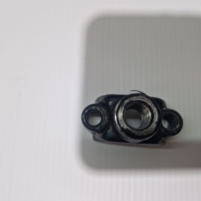 Peça mecânica metálica pequena com orifícios de fixação sobre superfície branca