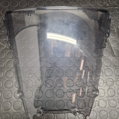 Para-brisas transparente curvo com furos de fixação em superfície preta com padrão circular