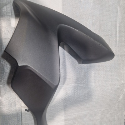 Peça plástica preta angular sobre tecido claro com padrão de linhas verticais