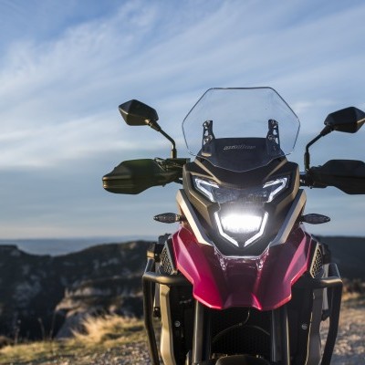 Motociclo vermelho e preto visto de frente com farol aceso em ambiente exterior