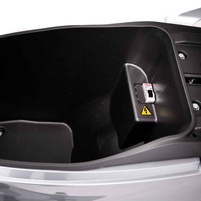 Depósito interno preto de scooter elétrica com interruptor e adesivo amarelo de aviso