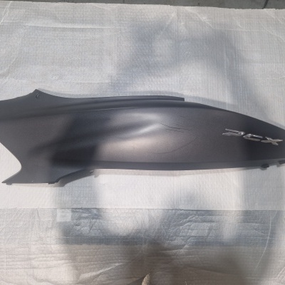 Peça lateral preta de mota com texto PCX numa superfície branca.