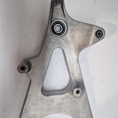 Peça metálica triangular com rolamento embutido em fundo branco texturizado