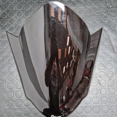 Para-brisa escuro em plástico com a palavra 'Ermax' e fundo metálico com padrão circular