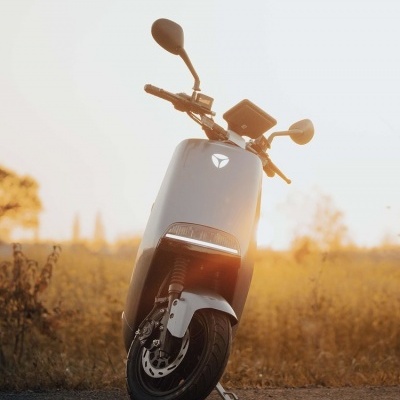 Scooter elétrico cinzento em estrada com fundo de vegetação ao pôr do sol