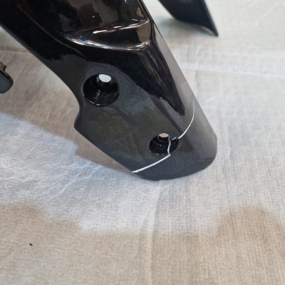 Peça plástica preta brilhante com orifícios, sobre tecido cinzento