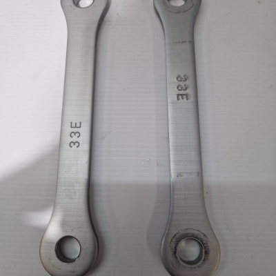 Duas peças metálicas prateadas com orifícios nas extremidades e inscrição 33E.