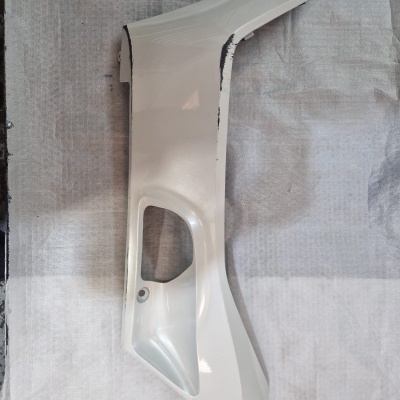 Peça lateral branca para mota ou scooter com buraco funcional e danos na borda, sobre fundo claro