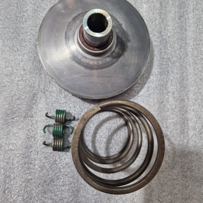 Componentes metálicos industriais incluindo disco cónico, molas helicoidais verdes e molas circulares sobre superfície cinzenta.