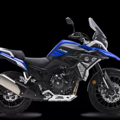 Motocicleta azul e preta com silenciador metálico e para-brisas transparente sobre fundo negro