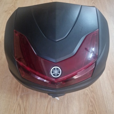 Top case preto com detalhe vermelho e logótipo Yamaha sobre chão de madeira