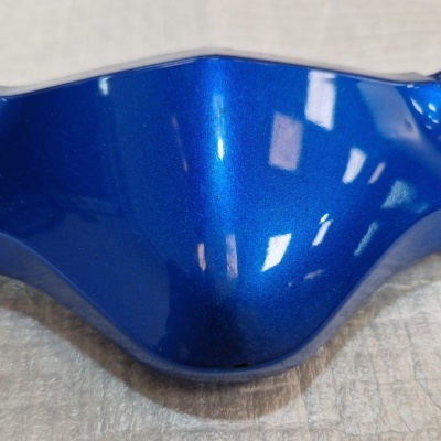 Peça plástica azul metálica brilhante sobre superfície clara texturada