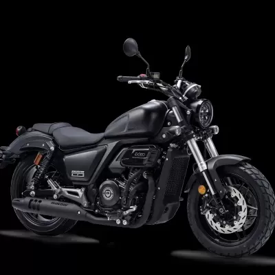Motocicleta preta com acabamento mate, banco de couro, pneus largos e farol redondo.