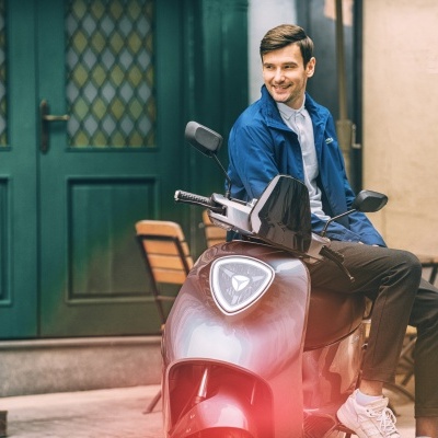 Homem sentado numa scooter vermelha e preta numa rua urbana