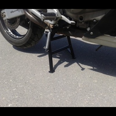 Suporte central de mota preta e roda traseira sobre pavimento de cimento