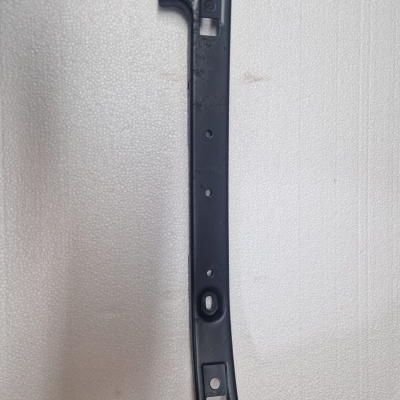 Peça metálica preta longa com orifícios sobre superfície branca