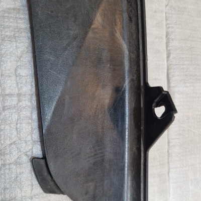 Peça de plástico preta com formato alongado sobre superfície têxtil clara