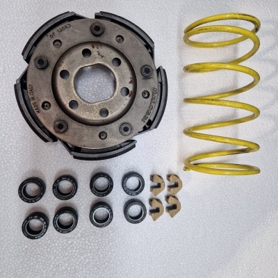 Peças de embraiagem e mola amarela sobre fundo branco texturizado.