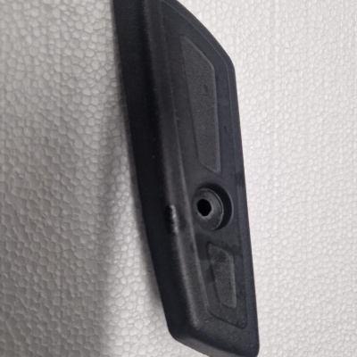 Peça preta de plástico com furo central e textura geométrica sobre superfície branca