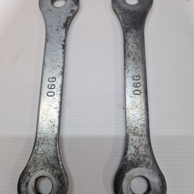 Dois elementos metálicos com dois orifícios e marcas 0GG e 0GO sobre fundo branco.