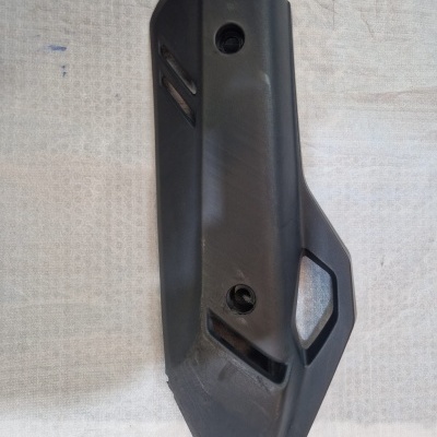 Peça de plástico preta com furos de fixação sobre tecido branco.