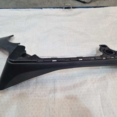 Peça automóvel preta em plástico com várias aberturas sobre tecido branco