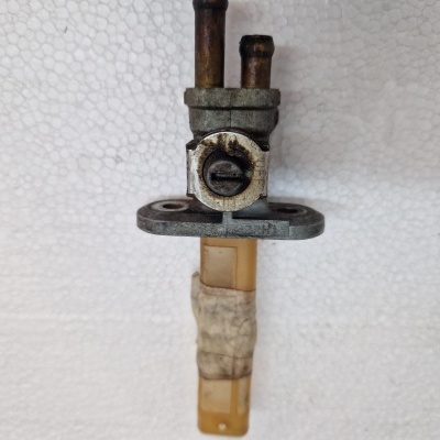 Peça metálica e plástica com duas tubagens de cobre e fita adesiva em fundo branco