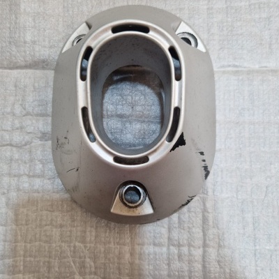 Peça metálica prateada com orifício oval central e desgaste