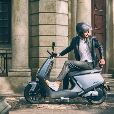 Scooter elétrico cinza metálico estacionado junto a edifício com colunas