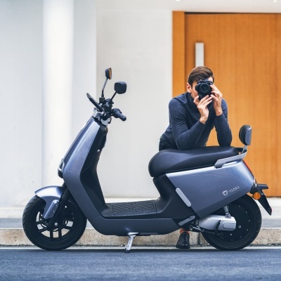 Moto elétrica cinza escura com homem a tirar foto sentado num banco da moto