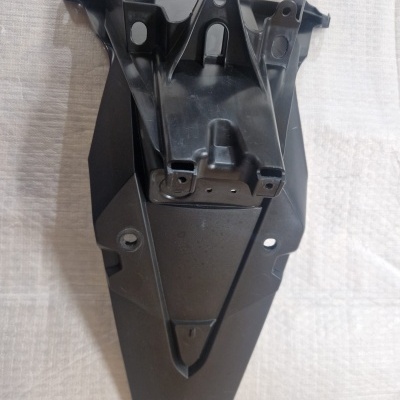 Peça de plástico preta para veículo com orifícios de fixação sobre pano branco