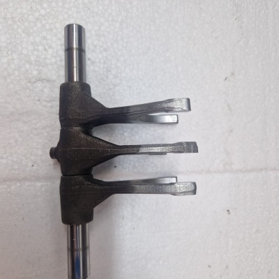 peça metálica com três braços e dois eixos cilíndricos sobre superfície branca