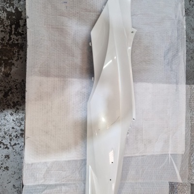 Peça lateral de moto branca em fundo branco e chão cinza