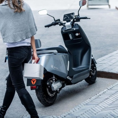 Moto elétrica cinzenta estacionada numa calçada junto a uma pessoa a caminhar