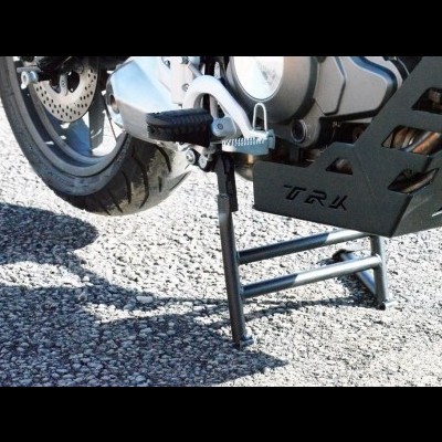 Detalhe da moto preta com suporte lateral e inscrição TRK sobre asfalto