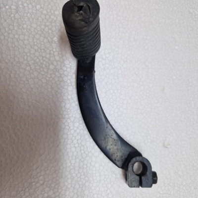 Pedal metálico preto com borracha canelada, visto de frente sobre superfície esferovite