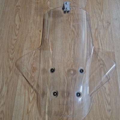 Para-brisas transparente para motocicleta colocado sobre chão de madeira clara