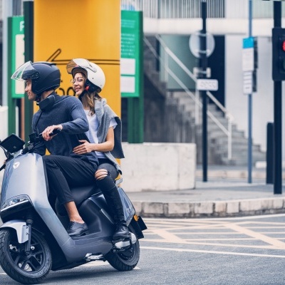 Duas pessoas numa scooter elétrica cinza num cruzamento urbano