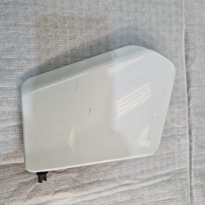 Peça de plástico branco trapezoidal com conector preto sobre tecido cinzento