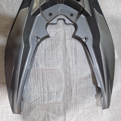 Peça plástica cinza e preta para motocicleta sobre tecido branco