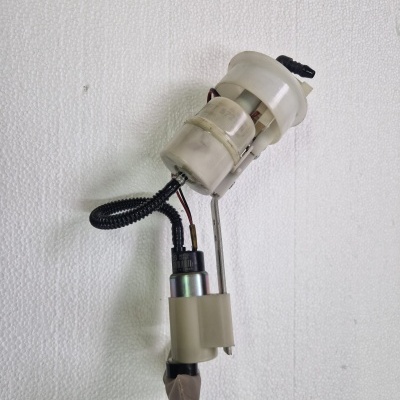 Bomba de combustível automóvel com componentes plásticos e metálicos, fios isolados e fita adesiva numa parede branca.