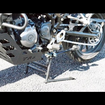 Moto preta com detalhes metálicos e suporte lateral num pavimento de cascalho