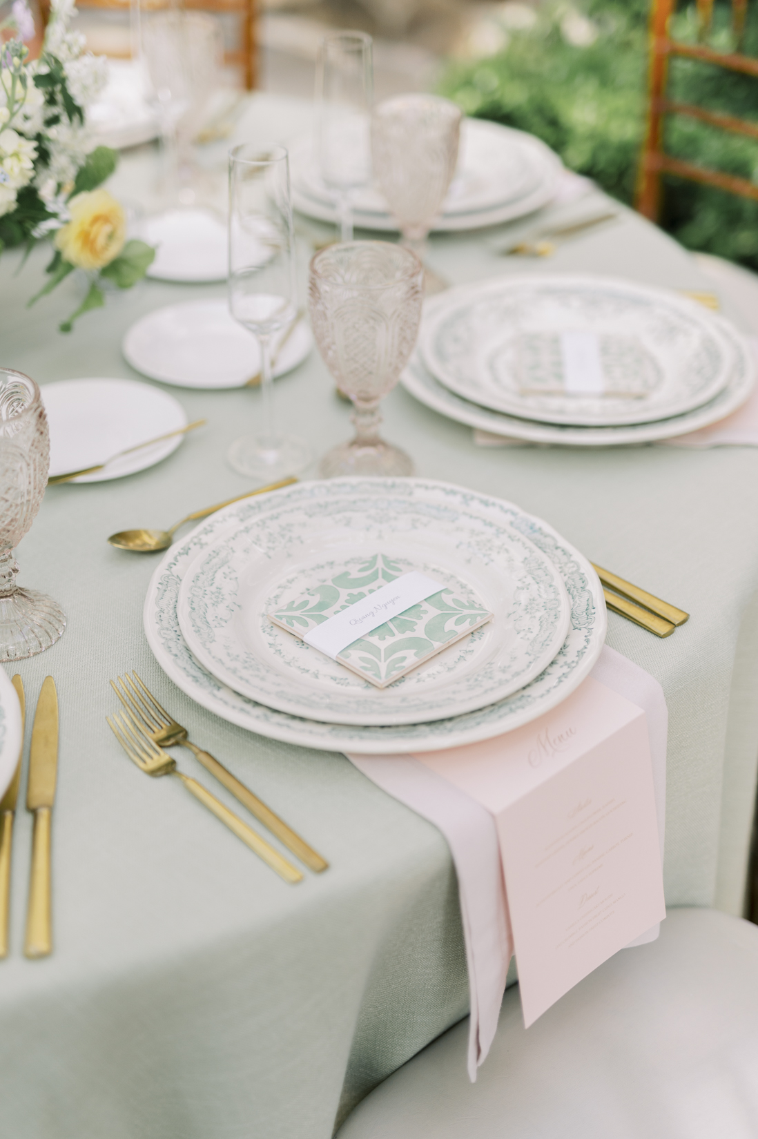 Mesa posta elegante com pratos brancos decorados, talheres dourados e copos de vidro texturizado