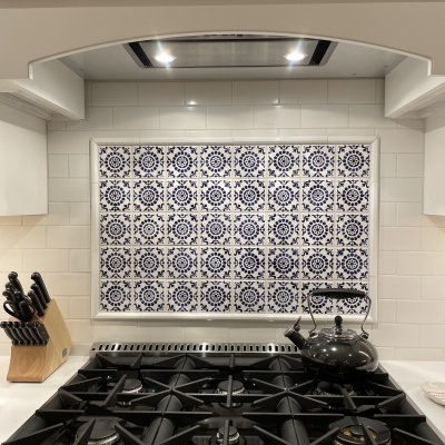 Fogão preto com jarro de chá, suporte de facas e azulejos brancos e azuis ao fundo