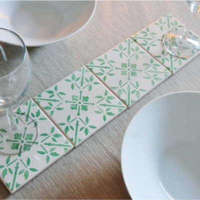Suporte de azulejos verdes e brancos com copos e pratos brancos numa mesa com toalha bege