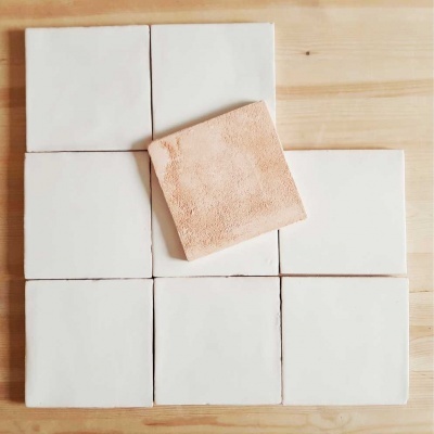 Azulejos quadrados brancos com um azulejo castanho claro no centro, sobre superfície de madeira clara.