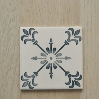 Azulejo quadrado branco com padrão geométrico azul e cinzento sobre madeira clara.